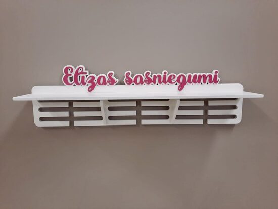 Medaļu stends, kausu plaukts baltā krāsā, ar rozā burtiem 