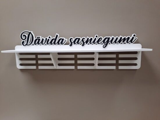 Medaļu stends, kausu plaukts baltā krāsā, ar melniem burtiem 